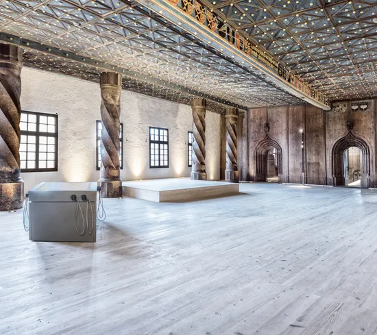 Historischer Saal mit verzierten Säulen, Holzboden und dekorierter Decke